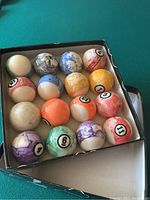 Complete set of marbled pastel billiard balls arranged in original box on green pool table.