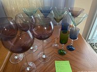 Photo showing a group of colored martini glasses and balloon wine glasses on a wooden surface with a sticky note listing the lot contents.
