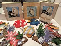 All items arranged on a flat surface showing three canvas art panels with seashells and multiple colorful metal fish and coral decorations.