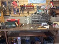 Overview of the wooden workbench with visible mounted tools above it, some tools and items on bench surface, and items stored beneath