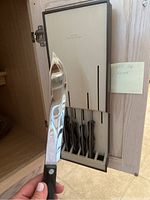 Person holding large chef’s knife removed from mounted block, showing blade curvature and handle details