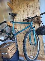 Full side profile of the Diamond Back mountain bike mounted on a wooden rack showing the frame, tires, pedals, and helmet hung on handlebar.