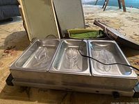 Full view of Oster food warmer with 3 stainless steel pans and clear lids, plus five extra warming plates.