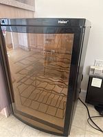 Front view of the Haier wine cooler with a closed glass door showing metal racks inside.