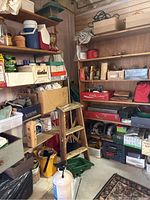 Wide view of shelves containing coolers, boxes, rope, household and workshop supplies, wooden step ladder, and plastic crates on floor.