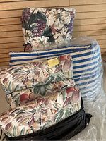 Overview photo showing three floral outdoor cushions stacked and one blue & white striped cushion in plastic bag, plus a square floral back cushion in the background
