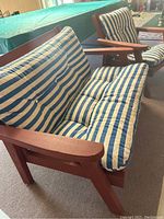 Front and side view of wooden outdoor loveseat and chair with blue and white striped cushions showing shape and cushions.