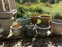 Photo of various resin and ceramic planters arranged outdoors on rocks and ground in sunlight.