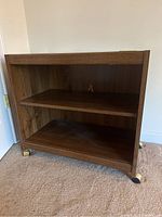 Front view of wooden rolling cart showing two shelves and caster wheels below