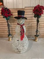 Wide view of the snowman figure flanked by two poinsettia topiaries, showing the height and style of all three items.