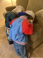 Two dolls in time-out position facing couch, showing back and clothing details.
