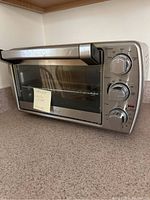 Oster toaster oven angled view showing front glass door and control knobs with a note on the door.
