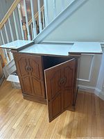 Wooden bar console cabinet with extending white top surface and two decorative front doors open revealing inner shelves