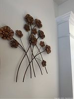 Front angle view of metal floral wall art showing flower petals and curved stems attached to a white wall.