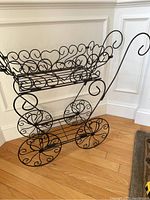 Side angle view of the black wire plant stand cart showing ornate scrollwork and large wheels.