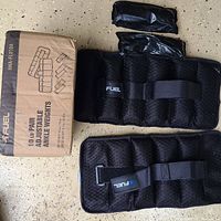 Pair of black adjustable ankle weights with removable weight packets next to original Fuel branded box