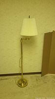 Full view of vintage brass tone metal floor lamp with pleated lampshade and visible horse finial on top