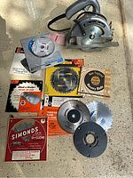 Full overview of Black & Decker circular saw and assorted saw blades including blades in packaging and loose blades on surface.
