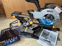 Full view of the Chicago Electric 10-inch sliding compound miter saw with owner's manual and extra 10-inch Hercules replacement blade visible.