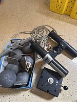 Downrigger weights, black rod holders, mounting base, and rope arranged on floor showing all items.