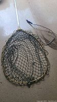Close-up image of large fishing net with metal pole and netting coiled inside frame, alongside small fishing net.