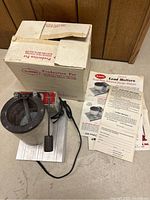 Photo showing the lead melter unit with original box and instruction leaflets arranged around it.