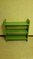 Front view of the mint green wooden book shelf showing three shelves and overall shape with some wear marks on the shelves and edges.