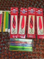 Four Northern King NK 28 fishing spoons in original packaging displayed alongside sets of colorful metallic fishing rod stickers with various patterns.
