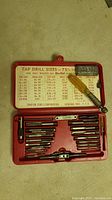 Full view of tap drill set in red plastic case showing taps, wrench, yellow screwdriver, adapter, and drill size chart inside lid.