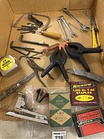 Full contents of the lot in a cardboard box showing various hand tools including clamps, wrenches, screws, and staples.