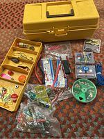 Full display of the yellow Old Pal tackle box open with multiple compartments and an assortment of fishing lures, terminal tackle, and accessories spread around.