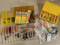 Full view of assorted vintage fishing lures, tackle boxes, packages of fishing line, and plastic bags containing soft lures and lure parts.