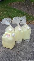 Four large rectangular pale yellow water jugs for outdoor use, three wrapped in plastic bags, one unpackaged, each with screw-on white caps and labels.