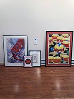 Four framed artworks arranged on floor against wall: Willard Bond sailboat print, large Asian inspired drum artwork, two smaller Asian inspired framed pieces.