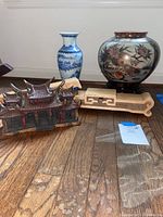 Photo showing two vases, one with blue and white landscape design, another large multicolor vase with floral and bird motifs, two wooden shelf stands, and a detailed wooden Asian building model.