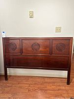 Full view of the dark solid wood headboard showing the three carved circular Asian inspired motifs along the top panel.