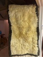 Full view of the cream color sheepskin rug with dark brown trim, showing rectangular shape and fluffy texture