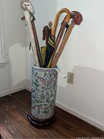 Full view of decorative ceramic umbrella stand holding various walking sticks and umbrella, showing floral and bird motifs and wooden base.