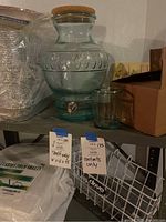 Glass beverage dispenser with cork lid and matching green glass cup on shelf