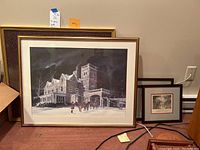 Framed artworks shown leaning against a wall including large framed winter scene and other smaller framed prints.