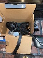 Panasonic Lumix camera and Nikon binoculars inside an open cardboard box showing lens caps and straps.