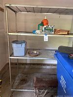 Metal storage shelf unit with items including bucket, work gloves, maintenance items, and seed bag on shelves.