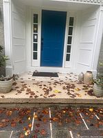 Photo of front porch with two planters near steps, decorative jug and vase on right, and welcome mat at door