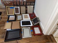 All picture frames arranged on wooden floor near brick fireplace and white wall