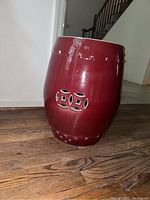 Side view of maroon porcelain garden stool showing decorative cutouts and rivet-like accents.