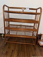 Front view of the brown rattan shelf showing four open rattan slatted shelves and the open frame sides