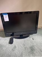 Front view of the 26 inch Vizio television with remote control beside it on a carpeted surface.