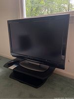 30-inch Sharp television with screen, remote control placed beside it, and black TV stand under the TV.