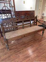 Full view of the vintage wooden bench showing carved backrest, rattan seat, and turned legs.