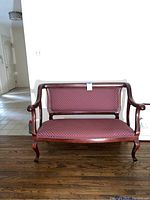 Front view of vintage wooden love seat with deep red patterned upholstery and curved arms and legs